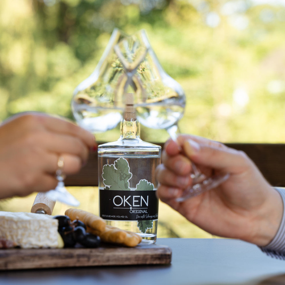 OKEN Original - Edelbrand aus Eicheln. Sehr mild, Aromen von Birne/Mirabelle und hellem Holz. Zwei Personen stossen an.